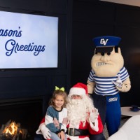 Little girl with multi-colored sweater on Santa's lap with Louie behind them